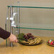 A person using an Advance Tabco food shield to protect a display of fruit, cookies, and chocolate covered strawberries.