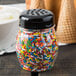 A Tablecraft black plastic perforated shaker top filled with sprinkles on a counter in an ice cream shop.