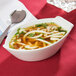 A CAC Super White porcelain boat bowl filled with soup with noodles and green onions.