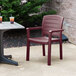 A Grosfillex Acadia Bordeaux Classic stacking resin armchair on a patio next to a table with drinks.