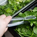 A hand using Thunder Group clear plastic tongs to pick up spinach.
