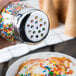 A hand uses a Tablecraft shaker to sprinkle sprinkles on a bowl of food.