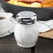 A Tablecraft salt shaker with a chrome-plated top next to a bowl of food.