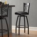 A Lancaster Table & Seating black finish cross back swivel bar stool with a black vinyl padded seat.
