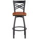 A black Lancaster Table & Seating bar stool with a cherry wood seat and cross back.