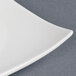 A close up of a CAC white divided tasting plate with a curved edge.
