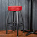 A Lancaster Table & Seating black bar stool with a red vinyl seat.