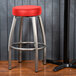 A metal Lancaster Table & Seating swivel bar stool with a red vinyl seat.