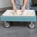 A person in gloves using a Cambro pizza dough box dollie to hold dough on a tray.