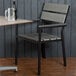 A BFM Seating black aluminum armchair with a gray synthetic teak back and seat next to a table with a beer bottle and a glass on it.