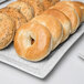 A rectangular porcelain platter with bagels and bread rolls on it.