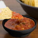 A black melamine salsa bowl with a chip dipped in salsa.