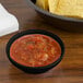 A black salsa bowl on a table of chips.