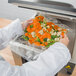 A person in a white lab coat using a VacPak-It chamber vacuum packaging bag to hold vegetables.