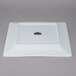A white square porcelain charger plate with a black label on a counter.
