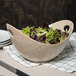 A 10 Strawberry Street Tiger Eye porcelain bowl with cut-out handles filled with lettuce on a table.