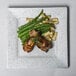 A 10 Strawberry Street blue speckled square porcelain dinner plate with meat and green beans on it.