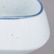 A close up of a white porcelain demi bowl with blue speckles.