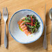 A plate of salmon and vegetables in a 10 Strawberry Street Arctic Blue porcelain bowl on a table with silverware.