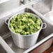 A Town aluminum colander full of broccoli in a sink.