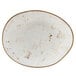 A white oval Tuxton China plate with brown specks on the rim.