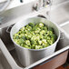 A Town aluminum colander filled with broccoli being washed in a sink.