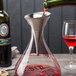 A glass container with a Franmara stainless steel decanter funnel filled with red liquid placed on a wine decanter.