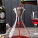 A Rabbit stainless steel wine shower funnel being used to pour red wine into a decanter.