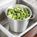 A Town aluminum colander filled with broccoli in a sink.