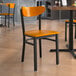 A Lancaster Table & Seating Boomerang Series black metal chair with a cherry wood seat and back on a table in a restaurant dining area.