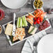 A Tuxton Kona Lava and Bright White rectangular china platter with cheese, crackers, grapes, and other food on a table.