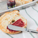 A person spreading jam on a bagel with a Oneida stainless steel butter spreader.