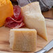 A 1/4 wheel of Parmigiano Reggiano cheese on a cutting board with meat.