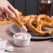 A hand holding a Dutch Country Foods soft pretzel over a bowl of dip.