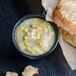 A bowl of Spring Glen Fresh Foods chicken corn soup with corn and spices next to a close up of bread.
