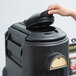 A hand putting a black lid on a black Cambro beverage dispenser.