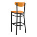 A Lancaster Table & Seating bar stool with a black finish and cherry wood seat and back.