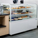 An Avantco glass top shelf for a bakery display case with pastries on it.