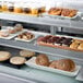 An Avantco shelf tag holder on a display case filled with pastries and pastries.