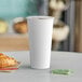 A close-up of a white Choice paper hot cup on a table with a croissant and coffee.