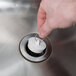 A hand using a white spiral rubber stopper in a metal sink.
