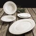A group of white Elite Global Solutions Della Terra Melamine irregular oval serving dishes on a wood table.
