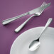 A Oneida Perimeter stainless steel table fork on a purple surface with a knife and spoon.
