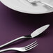 A close-up of a Oneida Apex stainless steel fish fork on a purple surface.