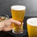 A hand holding a Libbey pilsner glass of beer.