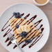 A plate with a crepe topped with bananas and blueberries with a fork and a cup of coffee on the side.