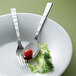A Oneida Verge stainless steel butter knife on a plate with a tomato and lettuce.