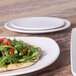 An Elite Global Solutions Tenaya off white melamine plate with a flatbread and salad on it next to a plate of pizza.