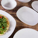 A close-up of a white Elite Global Solutions Tenaya square melamine plate with food on a wood table.