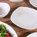 An Elite Global Solutions off white square melamine plate on a wood table with white bowls and plates.